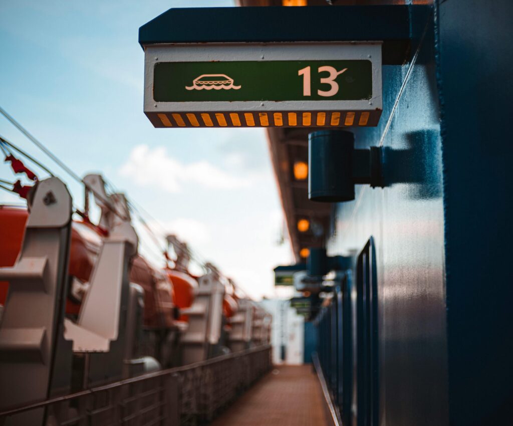 Close-up of a ship deck showing a green sign with a lifeboat symbol and the number 13.